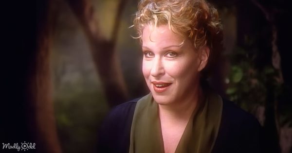 Bette Midler on stage, with a landscape in the background, performing 'From A Distance.'