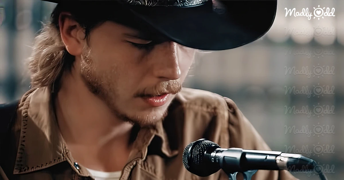 Colter Wall in a black hat and brown jacket in front of the mic and with guitar.