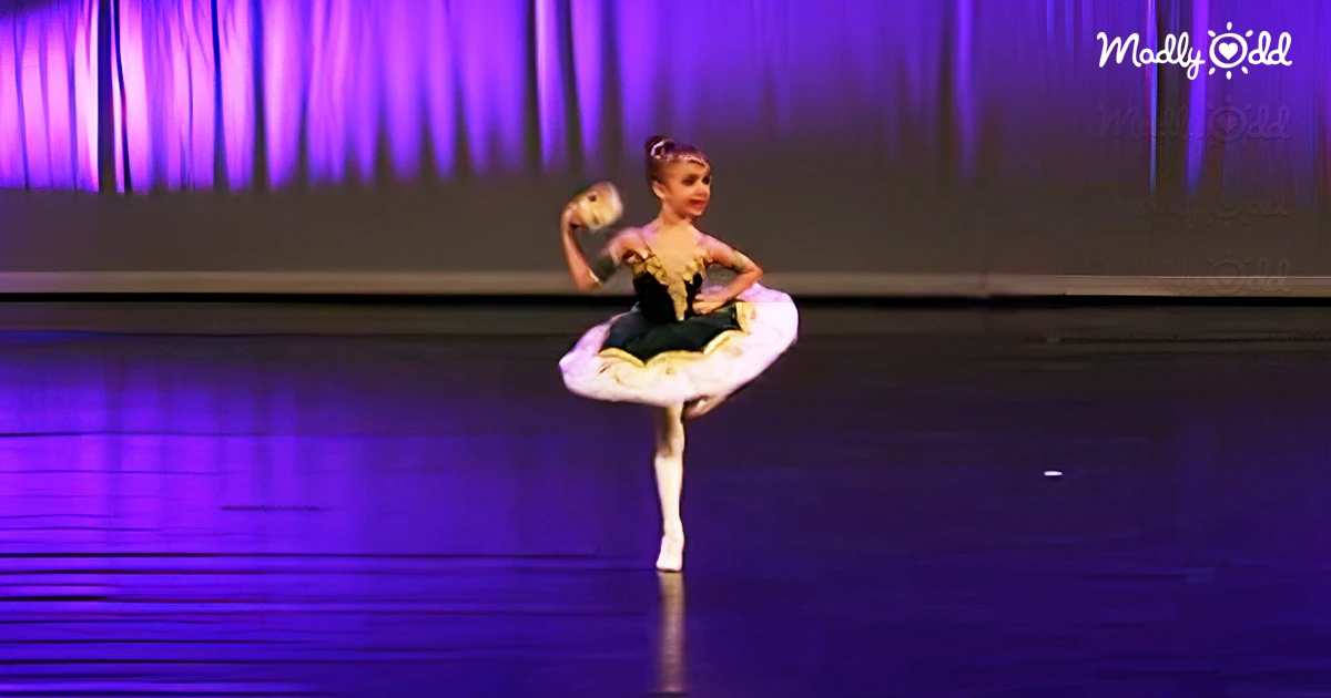 Young ballerina performs with astonishing control, purple light in background, reflecting off stage floor.